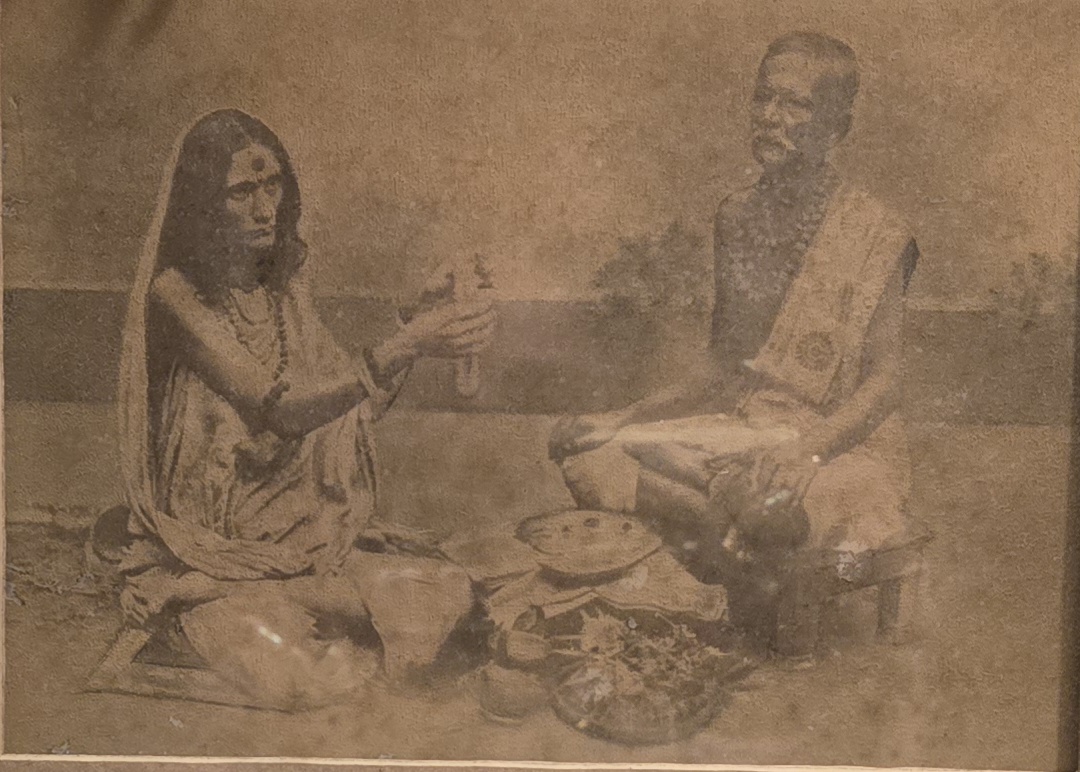 The great-grandparents of Meenakshii seated at puja — a sepia-toned ritual photograph