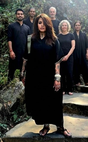 Meenakshii standing in front, five practitioners ranged behind her on stone steps in a hill setting